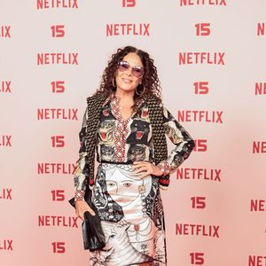 Carolina Ferraz: veste um conjunto estampado composto por blusa de mangas compridas com ilustração de tigres no busto e saia de comprimento mídi com ilustrações artísticas, acompanhado de xale de tricô sobre os ombros, óculos escuros e sandália de salto