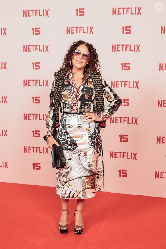 Carolina Ferraz: veste um conjunto estampado composto por blusa de mangas compridas com ilustração de tigres no busto e saia de comprimento mídi com ilustrações artísticas, acompanhado de xale de tricô sobre os ombros, óculos escuros e sandália de salto