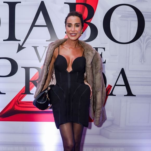 Carol Marra posou com um vestido preto curto de silhueta arquitetônica, apresentando um decote profundo em 'V' com recortes estruturados no busto e detalhes de volume nos quadris. Sobre os ombros, ela utilizou um casaco de pele (ou faux fur) em tom de marrom taupe
