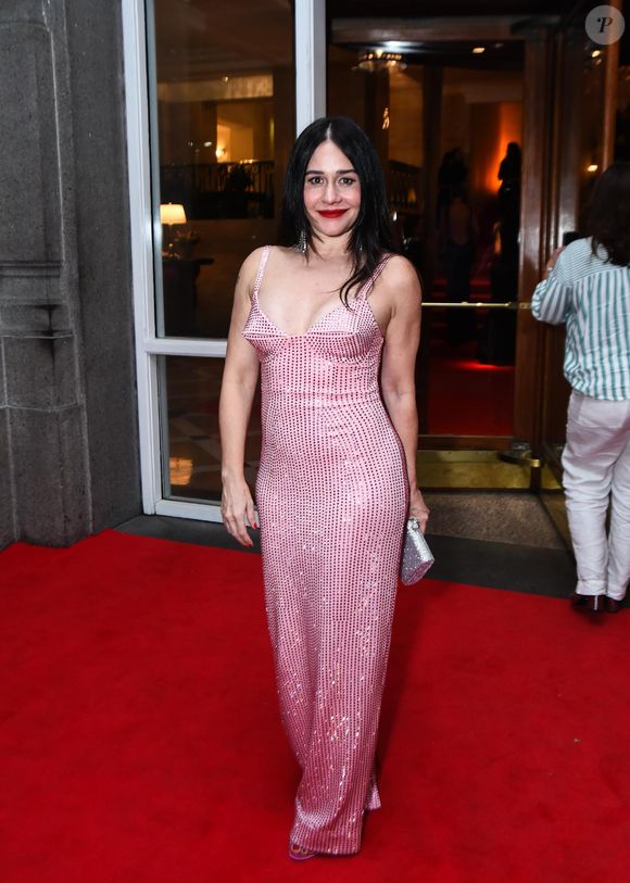 Alessandra Negrini optou por um vestido longo de alças finas inteiramente revestido por cristais ou paetês em tom rosa claro cintilante. O design apresenta um decote estruturado em formato de cone, remetendo a uma estética retrô e audaciosa. A peça possui modelagem reta que acompanha o corpo até o chão