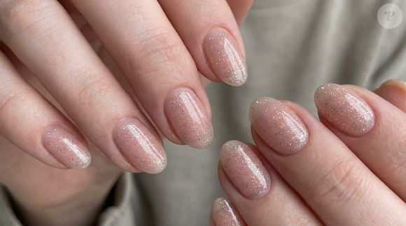 O glitter prateado sobre base nude rosada moderniza a manicura neutra com brilho frio e contemporâneo, ideal para peles de tom frio