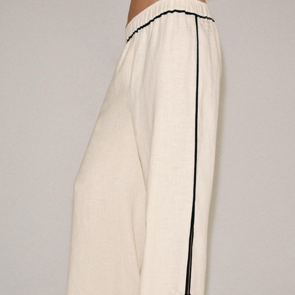 A calça de linho surge como uma das apostas para a Primavera 2026, com modelagem ampla, cintura média, cós elástico e fendas laterais que deixam a peça mais fresca para os dias de calor no Brasil. O detalhe de debrum em contraste acrescenta um toque sofisticado ao visual. Na Zara, custa R$ 439