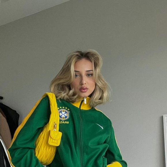 Tendência brasilcore de volta na Copa do Mundo de 2026: Malu Borges apostou em um casaco da Brazil national football team combinado com jeans e bolsa amarela, criando uma produção com irresistível vibe retrô e cheia de personalidade para torcer pelo Brasil com estilo