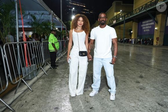 Rafael Logan e Natália Gibson apostaram em um visual coordenado em tons neutros e casuais. Natália vestiu regata branca ajustada com calça cargo ampla branca e bolsa tiracolo preta da Gucci com alça de corrente, enquanto Rafael optou por camiseta básica branca, calça jeans reta em lavagem clara e tênis brancos estilo casual