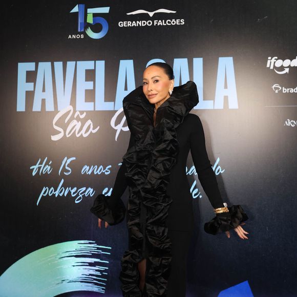 Sabrina Sato ousou com um vestido preto escultural e dramático, que trazia uma grande gola estruturada, mangas longas e uma fenda profunda, revelando uma bota over-the-knee também preta