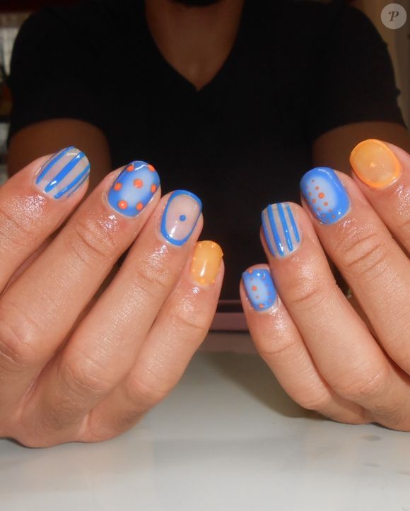 O Airbrush & Transparência traz uma referência diretamente ligada à estética Y2K. A proposta mistura esmaltes azul e laranja com efeito degradê e aerógrafo, além de transparências, poás e listras finas. O visual fica moderno pela combinação de elementos delicados e detalhes gráficos