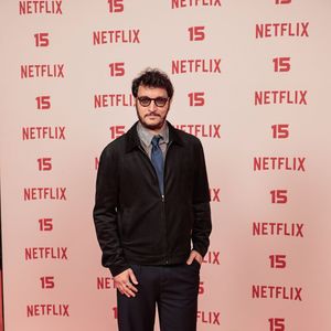 Alan Souza: vestido com uma jaqueta curta preta de fecho frontal sobre camisa cinza e gravata azul-marinho, calça social de corte reto escura e sapatos pretos