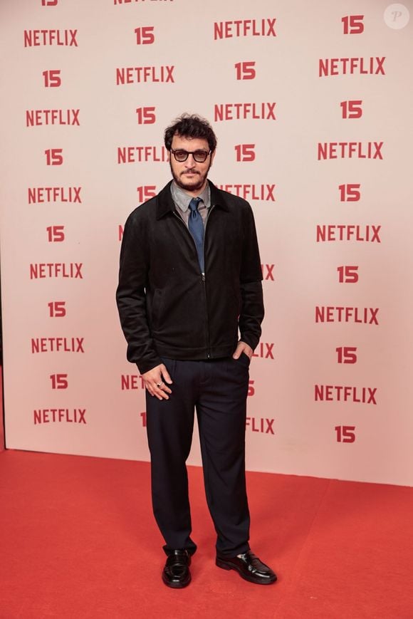 Alan Souza: vestido com uma jaqueta curta preta de fecho frontal sobre camisa cinza e gravata azul-marinho, calça social de corte reto escura e sapatos pretos