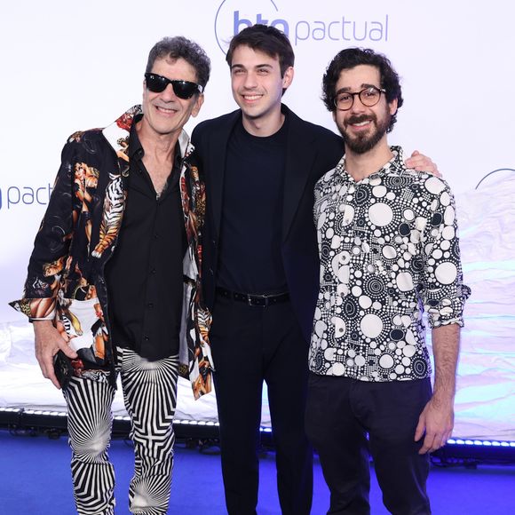 Jorge Israel, Dani Flomin e Leo Israel: Jorge (à esquerda) combina blazer estampado com tigres, calça de padronagem geométrica psicodélica em preto e branco e óculos escuros. Dani (ao centro) usa terno azul-escuro minimalista com camiseta e tênis branco. Leo (à direita) veste camisa de botões com estampa de círculos preto e branco e calça jeans escura