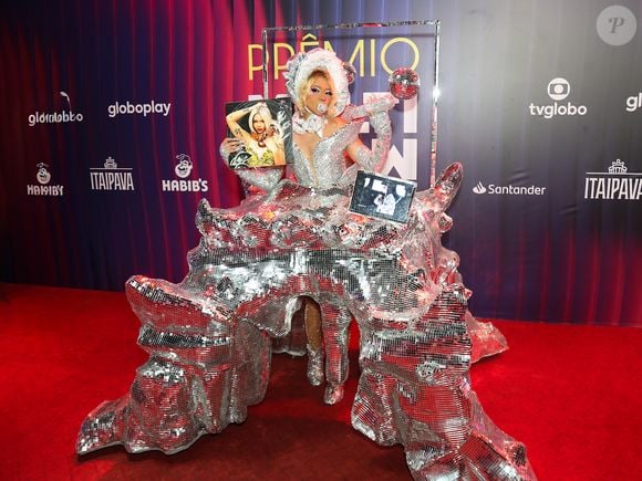 Com um body prateado superbrilhante, recortes ousados e uma cabeça cenográfica que mistura diva cyber com rainha disco intergaláctica, ela ainda carregou um quadro com sua própria foto, um tablet acoplado mostrando imagens e uma mini bola de espelhos! O resultado é uma figura que parece saída de um crossover de RuPaul’s Drag Race, Lady Gaga e arte pop futurista