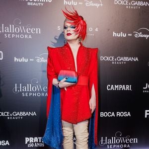 Lorelay Fox: o visual é uma produção conceitual e vibrante. É protagonizado por um vestido-paletó vermelho estruturado com ombreiras marcantes, profundamente cravejado de cristais vermelhos brilhantes e fendas laterais nas mangas que revelam um forro azul-brilhante