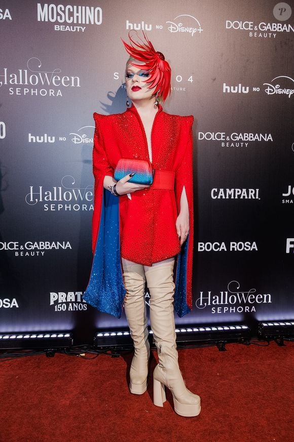 Lorelay Fox: o visual é uma produção conceitual e vibrante. É protagonizado por um vestido-paletó vermelho estruturado com ombreiras marcantes, profundamente cravejado de cristais vermelhos brilhantes e fendas laterais nas mangas que revelam um forro azul-brilhante
