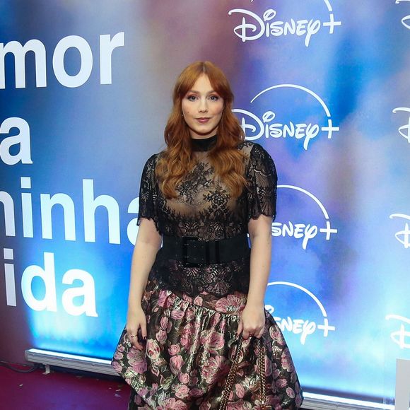 Malu Rodrigues: combina blusa de renda preta com transparência e gola alta a uma saia longa estampada em tons florais e metalizados, ajustada na cintura por um cinto largo de fivela
