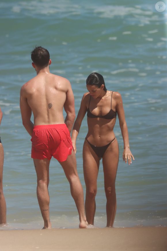 Bruna Marquezine, de fio-dental, renovou o bronzeado e se refrescou com João Guilherme (na foto de bermuda vermelha) em dia de praia no Rio