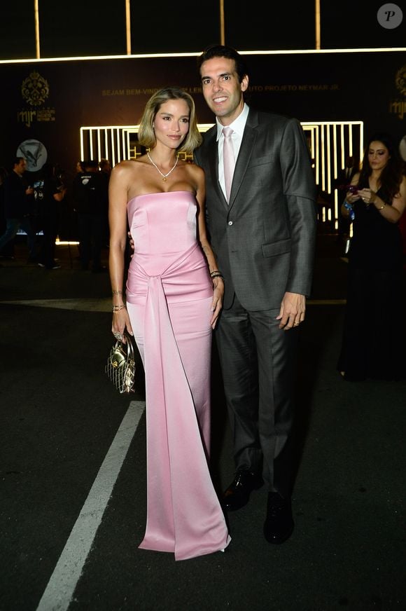 Carol Dias e Kaká: Carol optou por um vestido longo tomara que caia rosa-quartzo em cetim, com nó drapeado na cintura e fenda com caimento fluido; Kaká vestiu um terno cinza-chumbo com camisa branca e gravata rosa-claro em tom coordenado