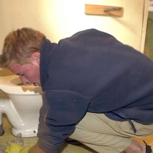 Príncipe William aparece ajoelhado e em posição de quatro, enquanto limpa um vaso sanitário. Foto foi tirada no Chile durante um trabalho voluntário