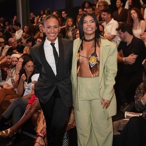 A dupla do BBB 26, Maxiane e Marciele, apresentou contrastes complementares na fila A. Maxiane (à esquerda) optou por um visual tomboy clássico e extremamente elegante, vestindo um terno preto de lapelas acetinadas combinado a uma camisa branca rigorosamente fechada e gravata preta fina. Já Marciele (à direita) trouxe a força da moda ancestral e brasileira, vestindo um conjunto de alfaiataria oversized em tom verde-pistache