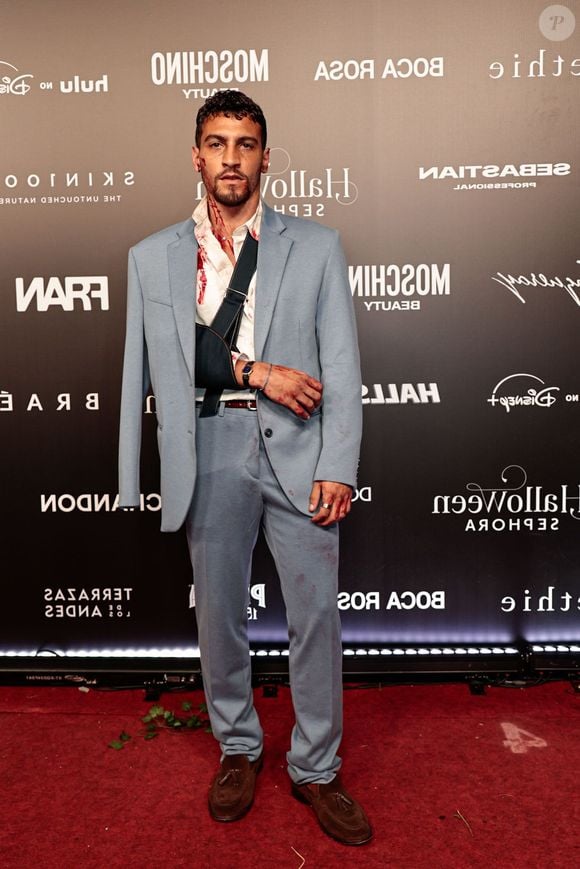 Henrique Barreiras veste um fato azul-claro com camisa branca desabotoada e sapatos mocassins castanhos de camurça. A produção de estilo dramático inclui manchas artificiais de sangue na camisa, no fato, no pescoço e nas mãos, acompanhadas por um braço imobilizado com uma tipoia preta