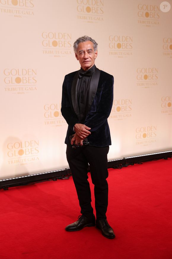 Chico Diaz escolheu um smoking com blazer de veludo azul-marinho, cujas lapelas em cetim preto criam um jogo de luz elegante sob os flashes. Fugindo da camisa branca óbvia, ele optou por uma camisa social preta inteiramente fechada, acompanhada de uma gravata borboleta de seda no mesmo tom