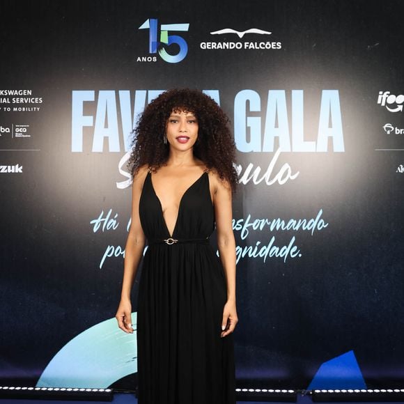 Taís Araújo: atriz aposta na elegância fluida de um vestido longo preto com decote V profundo e caimento esvoaçante. O modelo traz alças finas com detalhes metálicos dourados e cinto delicado com fivela combinando, que marca com precisão a cintura. Ela arremata o visual com joias discretas e batom escuro em tom vinho