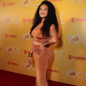 Lucy Ramos destaca a gestação com sofisticação em um conjunto de duas peças em tom caramelo, composto por crop top e saia longa drapeada com fenda lateral. O look ganha impacto com múltiplos braceletes dourados nos dois pulsos e sandálias de tiras finas tom sobre tom