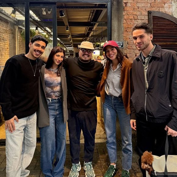Bruna Marquezine em foto com João Guilherme e amigos usando calça jeans mom jeans em lavagem mais clássica, aliando com t-shirt listrada, casaco em tom terroso, bom para o Outono, sem esquecer do boné e do tênis verde Samba da Adidas.