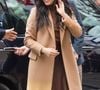 Meghan Markle mostra outra possibilidade de styling ao combinar tons terrosos e alfaiataria, com trench coat bege ou camelo, blusa de tricô marrom-café e saia midi de cetim marrom-fechado