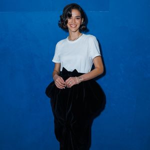 Bruna Marquezine exibe look sofisticado com camiseta branca, saia longa de veludo preto, laço volumoso na cintura e scarpin preto de bico fino