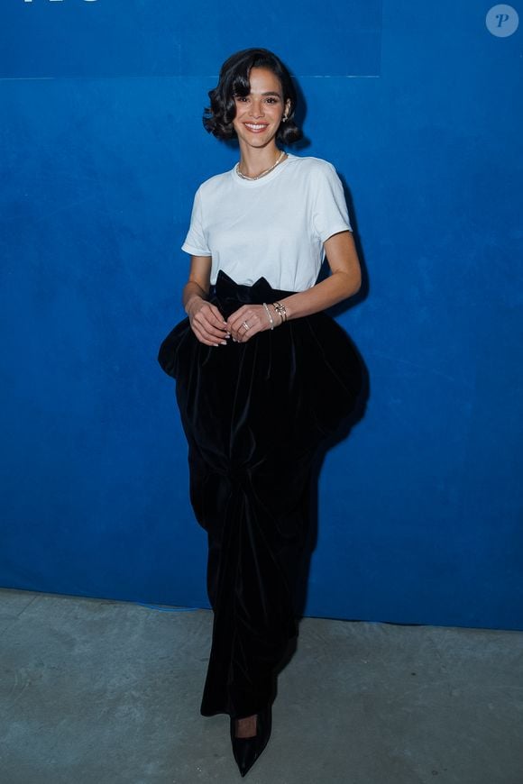 Bruna Marquezine exibe look sofisticado com camiseta branca, saia longa de veludo preto, laço volumoso na cintura e scarpin preto de bico fino