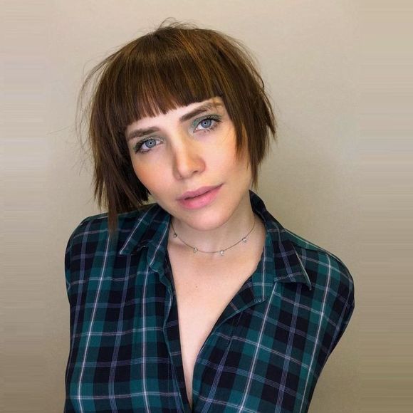Cabelo de Letícia Colin feito por Neandro Ferreira: um Short Bob ou French Bob super texturizado e bagunçado (messy). Tem uma franja reta desfiada e irregular na altura das sobrancelhas. O corte é desfiado nas pontas na altura do maxilar. O castanho escuro tem luzes muito finas e sutis em tom chocolate