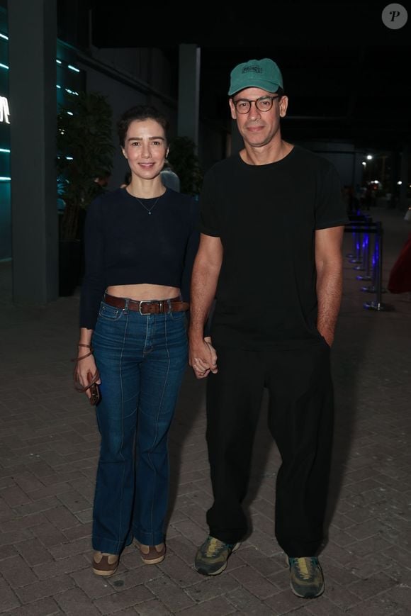 Marjorie Estiano apostou em um visual alinhado e casual ao lado do companheiro, vestindo um top cropped azul-marinho de mangas compridas e jeans de cintura alta com vinco frontal. Ela completou o look com cinto de couro marrom e sapatos num tom terroso elegante. Ao seu lado, ele vestia um look monocromático preto com camiseta básica, calça solta, tênis e boné verde