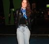 A atriz Nathalia Dill opta pelo contraste urbano combinando uma calça jeans reta de lavagem clara e cintura alta com uma jaqueta de couro preta em estilo biker. Por baixo da jaqueta, veste uma blusa preta sóbria, que ganha um ponto de cor marcante com um lenço de seda amarrado ao pescoço em tons de azul e branco, finalizando com botas pretas de amarrar