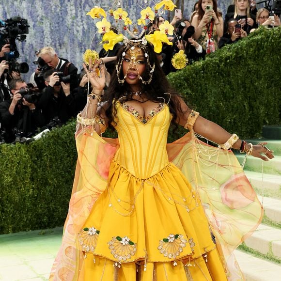 SZA: a cantora apresentou uma explosão de cor com um vestido amarelo vibrante inspirado na flora tropical. A peça contou com um espartilho estruturado e uma saia em camadas decorada com conchas bordadas, mas o grande destaque foi o adereço de cabeça: uma estrutura de arame dourado que suspendia orquídeas amarelas e detalhes em ouro, emoldurando seu rosto com uma delicadeza luxuosa
