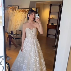 5. Linha A com aplicações florais em relevo (3D): vestido de noiva no corte linha A com corpete de decote coração levemente drapeado. O tecido de tule traz aplicações de flores e folhas em relevo 3D feitas do mesmo tecido, distribuídas de forma contínua a partir do peito até toda a extensão da saia volumosa