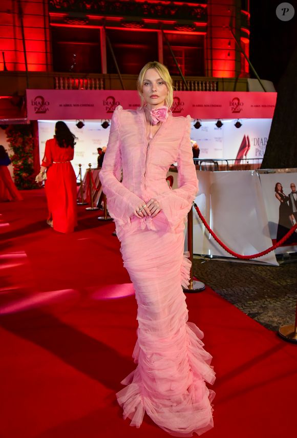Caroline Trentini: exalando o conceito high fashion, a top model utilizou uma criação monocromática em rosa pastel. O conjunto é marcado por camadas de tule drapeado e babados verticais que conferem uma textura densa e fluidez ao caminhar. O detalhe de destaque é a aplicação de uma flor gigante (corsage) no pescoço, tendência absoluta das passarelas internacionais. O blazer cropped com ombros estruturados equilibra a delicadeza da saia longa de sereia