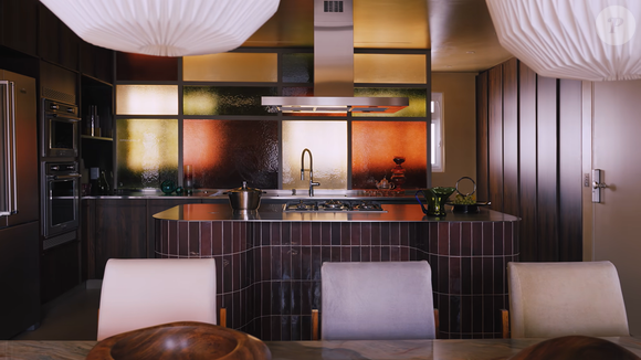A cozinha é um dos destaques do dúplex de Manu Gavassi e Jullio Reis, com marcenaria planejada, bancadas de aço inoxidável, ilha revestida de porcelanato e um painel de vidros coloridos em tons de âmbar, verde e laranja. Segundo a Casa Vogue, é nesse ambiente que a cantora costuma preparar panquecas de banana para a filha, Nara