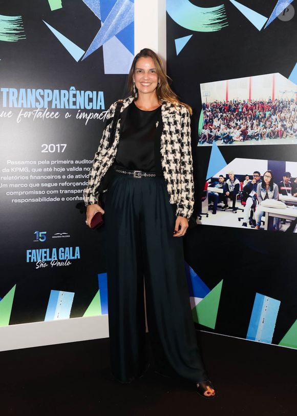Luciana Cardoso, esposa de Faustão usa look elegante e versátil: um blazer de tweed em preto e branco sobre um top de seda preto. Ela combinou as peças com calças pantalonas de cintura alta em verde esmeralda, realçadas por um cinto de couro preto com fivela metálica ornamentada. Ela completou a produção com sandálias pretas de salto e brincos longos e brilhantes