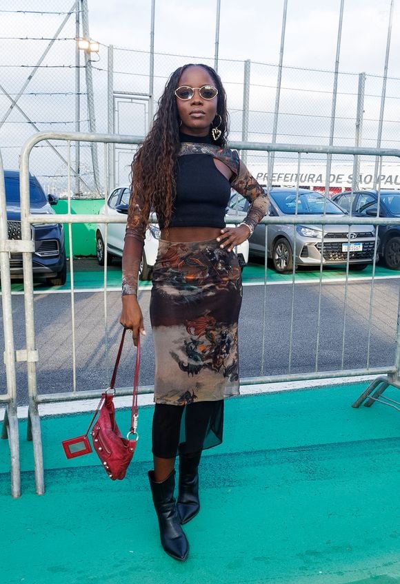 Para quem gosta de uma produção mais ousada, a inspiração é o look com tule e sobreposição. A composição da atriz Clara Moneke, reúne saia midi transparente com estampa artística e mística, usada sobre um short de alta compressão estilo biker, além de top assimétrico e mangas removíveis em tule