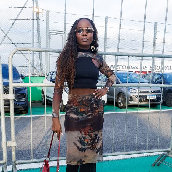 Para quem gosta de uma produção mais ousada, a inspiração é o look com tule e sobreposição. A composição da atriz Clara Moneke, reúne saia midi transparente com estampa artística e mística, usada sobre um short de alta compressão estilo biker, além de top assimétrico e mangas removíveis em tule