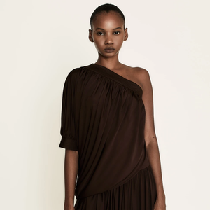 Look de Isabelle Drummond como Naiane na novela 'Coração Acelerado': a blusa apresenta caimento fluido com drapeado sofisticado, enquanto a saia com efeito plissado adiciona textura e modernidade ao visual