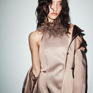 A peça que é a cara da influencer Naiane Amaral, em tecido que lembra cetim com acabamento acetinado chama atenção pela gola halter adornada com plumas, criando um visual sofisticado e ousado na medida certa