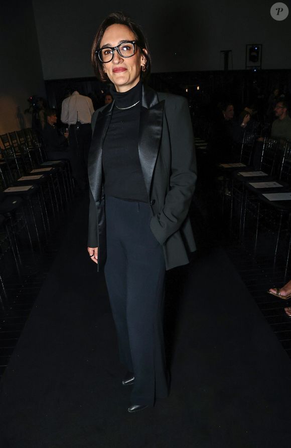 Maria Prata optou por um terno preto sofisticado de alfaiataria com lapelas acetinadas em estilo smoking, sobreposto a uma blusa de gola alta preta com gargantilha metálica discreta. A calça reta de corte amplo completa o visual monocromático, finalizado com óculos de armação preta marcante e sapatos escuros de bico fino