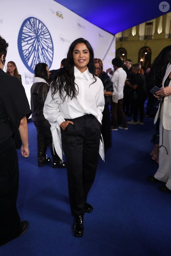 Lucy Alves: Visual moderno de alfaiataria composto por uma camisa social branca oversized com pontas alongadas e fendas nas mangas compridas. A peça foi usada por dentro de uma calça social preta de cintura alta com pregas, finalizada com sapatos de bico quadrado envernizados