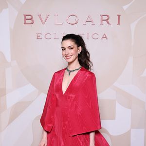 Anne Hathaway apostou em um vestido volumoso de alta-costura da Valentino, confeccionado em seda vermelha moiré, com decote profundo e uma capa elegante que caía sobre os ombros e costas