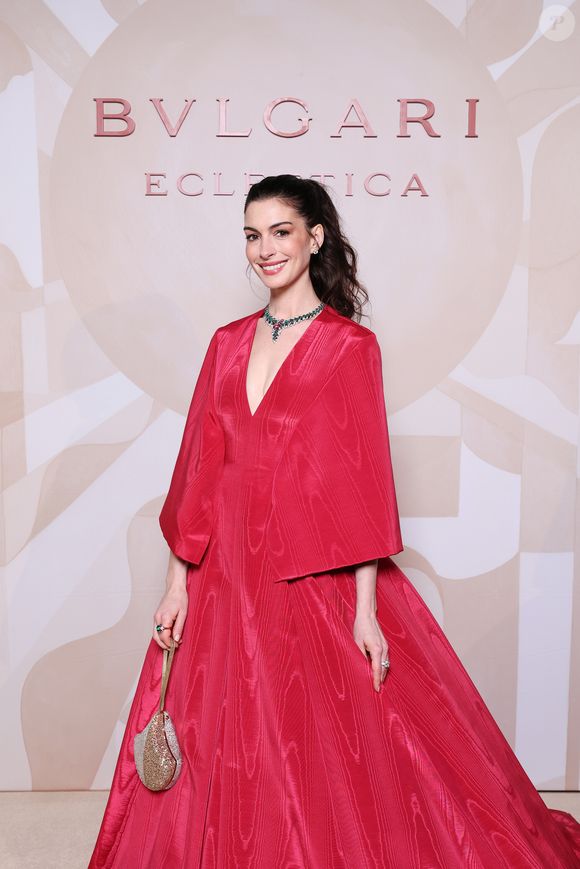 Anne Hathaway apostou em um vestido volumoso de alta-costura da Valentino, confeccionado em seda vermelha moiré, com decote profundo e uma capa elegante que caía sobre os ombros e costas