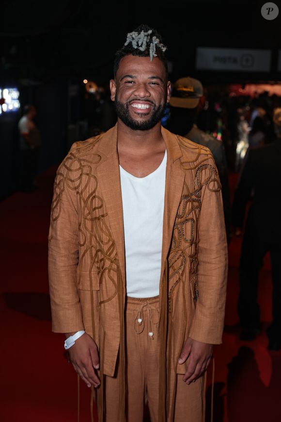 Rene Silva optou por um conjunto de linho em tom ferrugem que une conforto e elegância. O blazer longo possui aplicações de cordões bordados em padrões orgânicos que descem até a barra, criando um efeito visual de textura única. A calça, com amarração de cordão e detalhe de pérola na ponta, reforça o aspecto artesanal da peça
