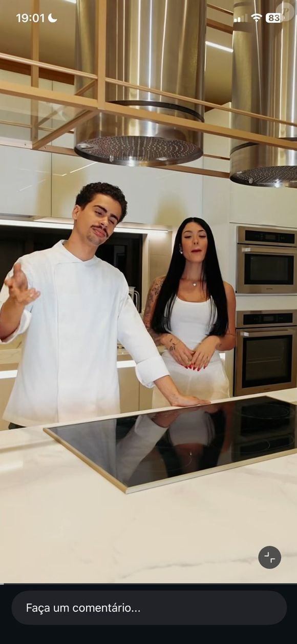 A cozinha tecnológica, usada por Rayane Figliuzzi em seus conteúdos de receitas, reúne cooktop de indução embutido, coifas de inox suspensas e eletros integrados em acabamento sofisticado