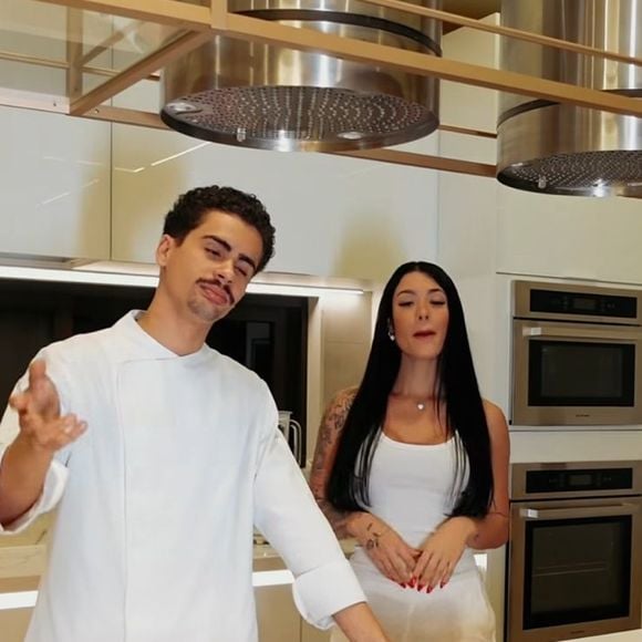 A cozinha tecnológica, usada por Rayane Figliuzzi em seus conteúdos de receitas, reúne cooktop de indução embutido, coifas de inox suspensas e eletros integrados em acabamento sofisticado