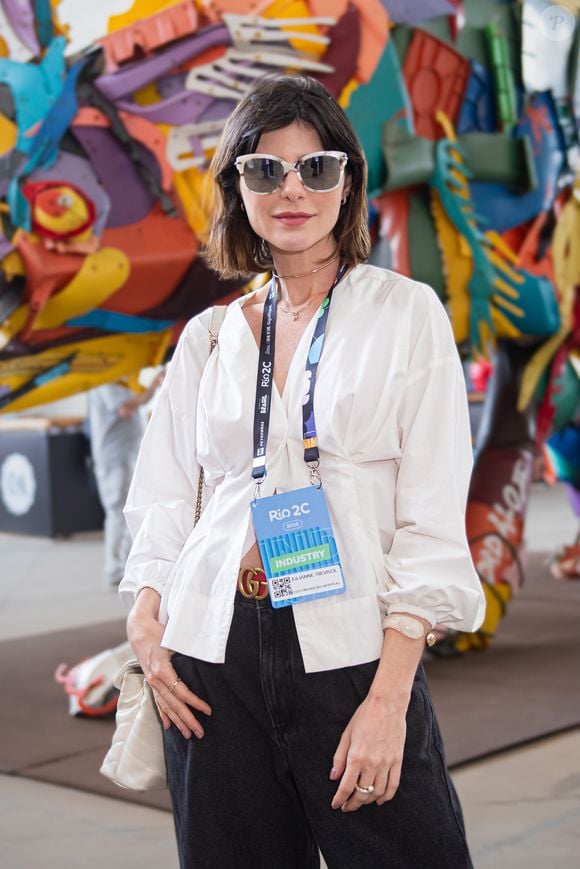 O visual da atriz Julianne Trevisol no Rio2C traz uma camisa branca texturizada com mangas bufantes e decote em "V", equilibrada por uma calça jeans preta de modelagem ampla