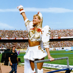 Xuxa Meneghel em uma de suas apresentações com look composto por ombreiras, bota branca, capa e minissaia.